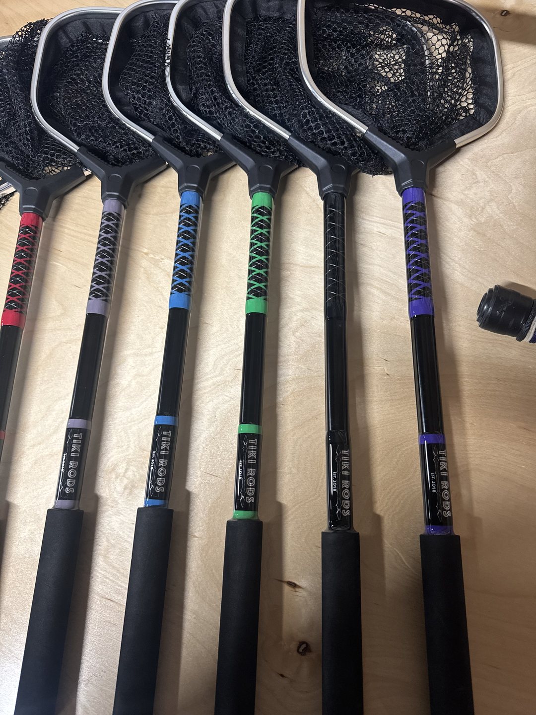 Six landing nets laid on a work table, their handles cross-wrapped in red, gray, blue, green, black and purple