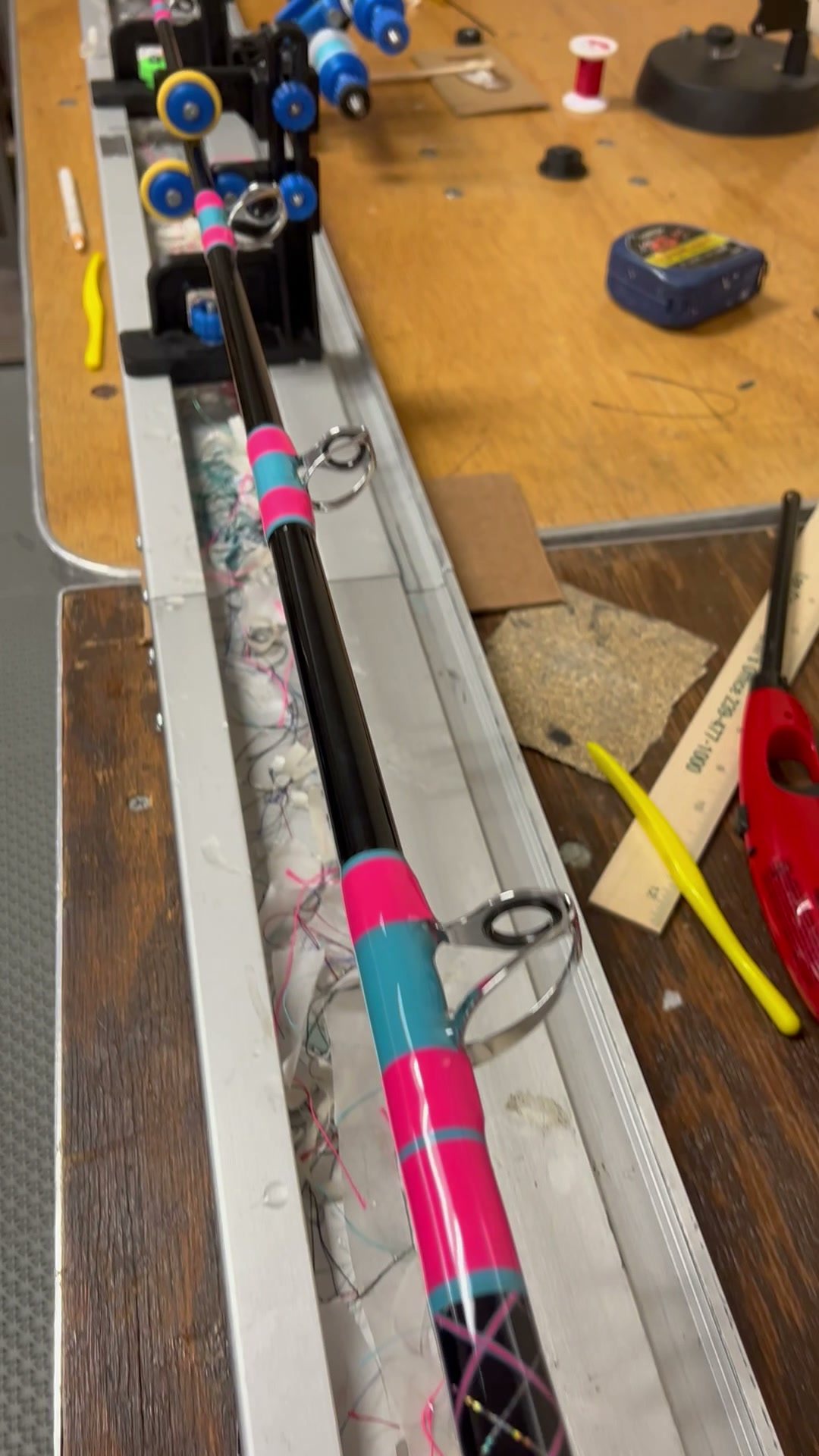 A blank on the wrapper, pink and teal thread already laid over the guide feet, spools and tools on the table behind